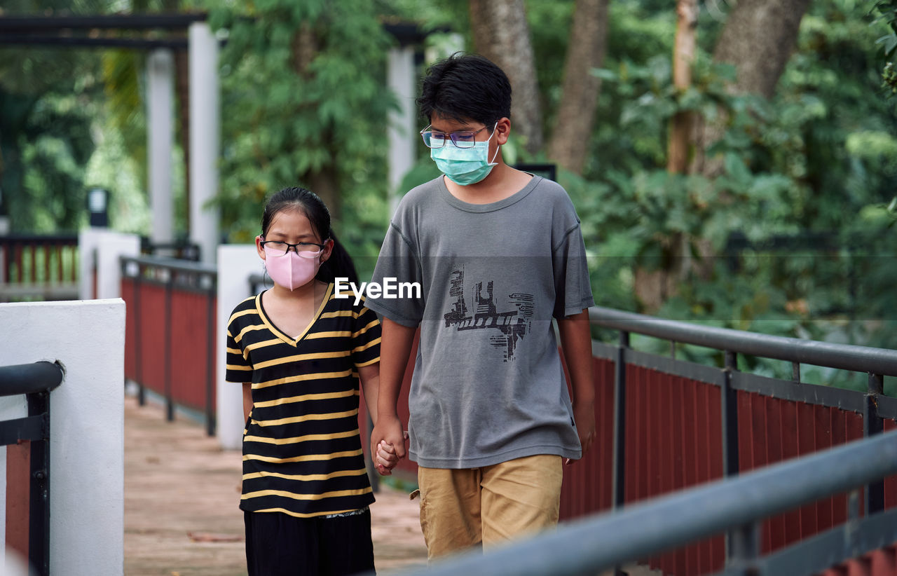 Brother and sister walking together in a public park during the covid-19 pandemic