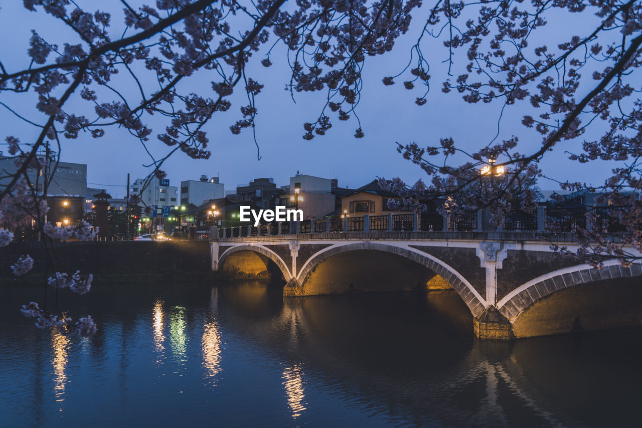 architecture, bridge, built structure, water, reflection, river, city, arch bridge, arch, illuminated, nature, tree, building exterior, transportation, travel destinations, sky, evening, dusk, night, plant, no people, cityscape, travel, outdoors, building, tourism, sunset, waterway, twilight, city life, history