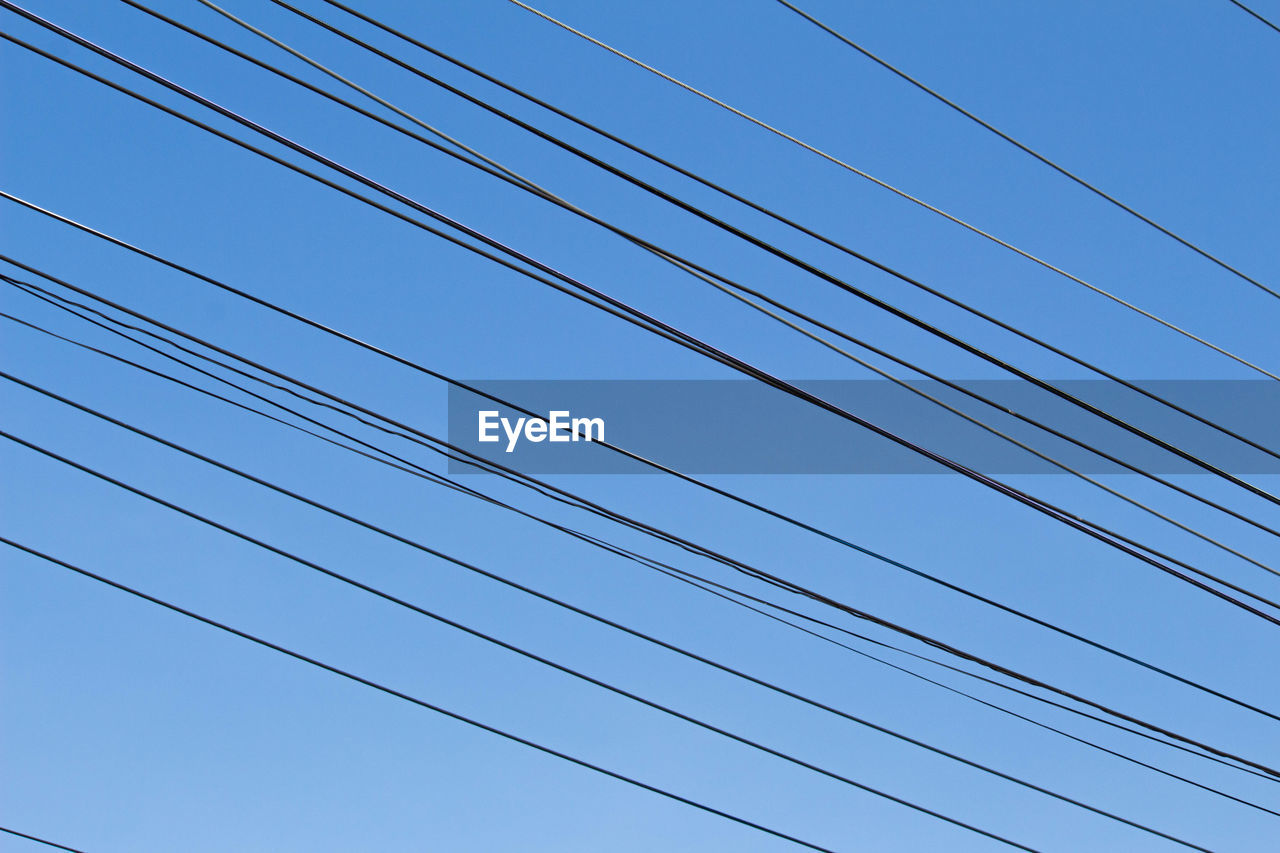 Low angle view of power cables against clear blue sky