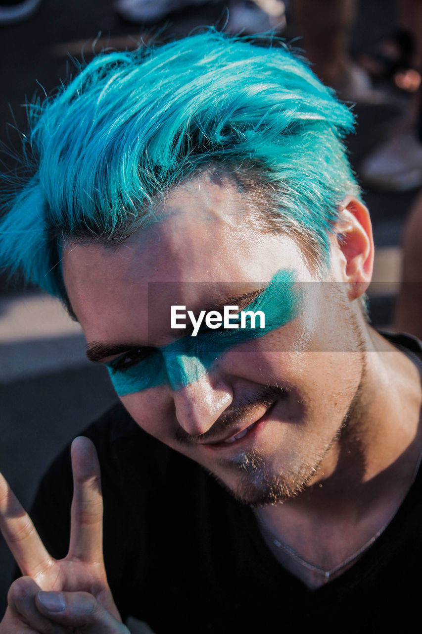 Close-up portrait of young man with dyed hair showing peace sign