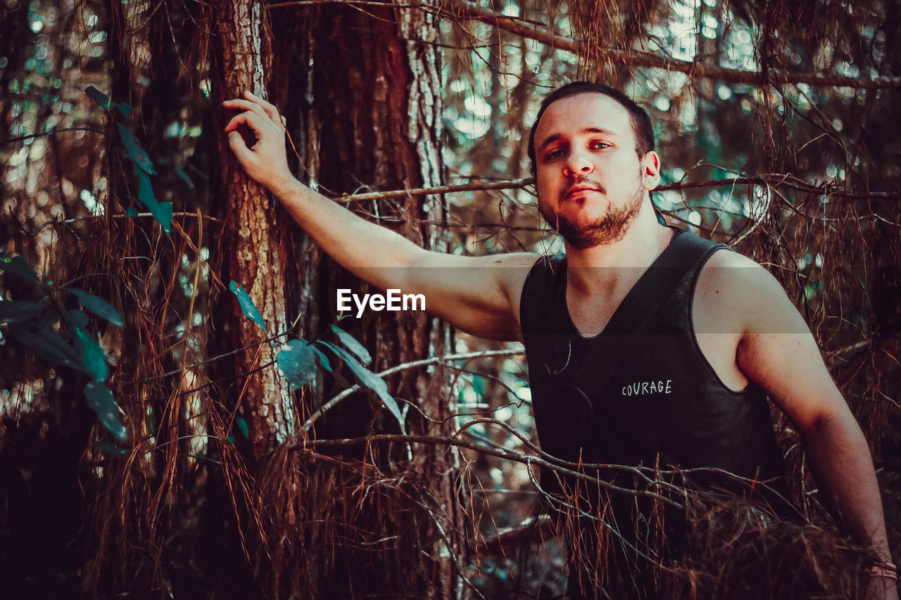 Portrait of man standing by tree trunk in forest