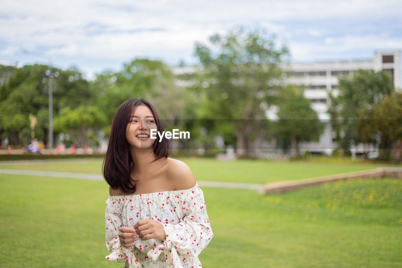 Young woman smiling while standing against at park