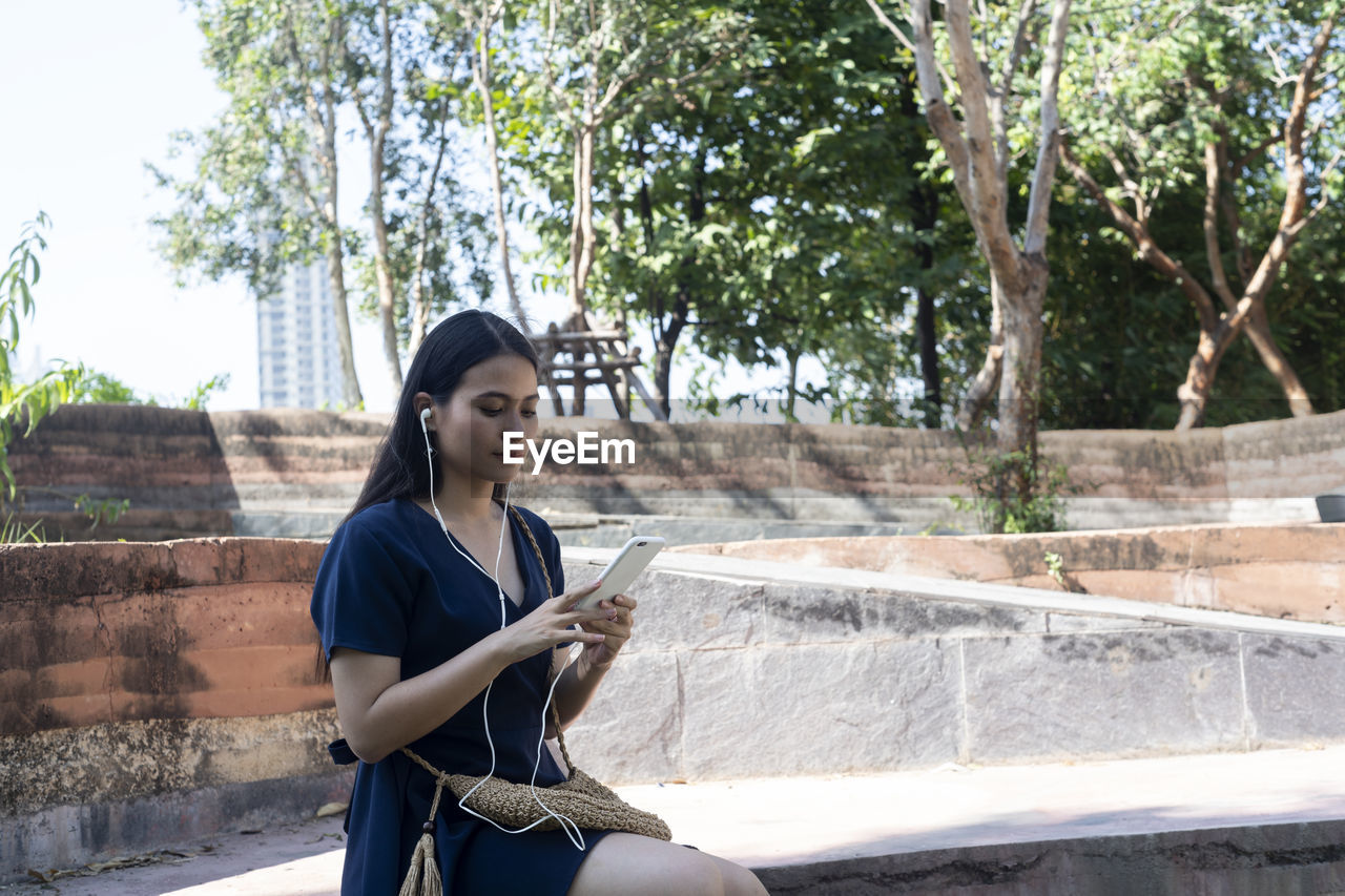 Long hair woman in dark blue dress type the answer into her smartphone and send it to her boyfriend.
