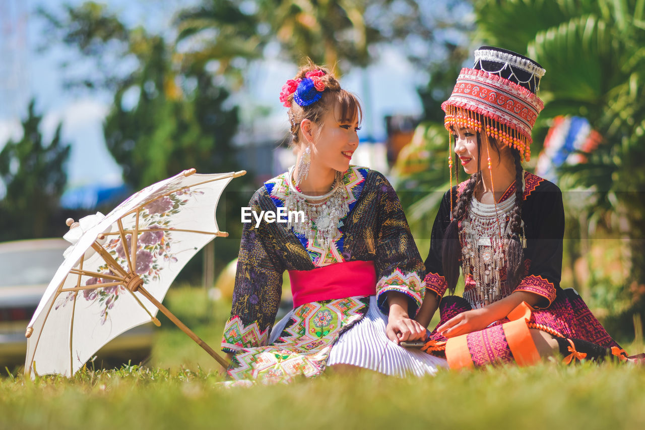 WOMEN SITTING ON FIELD BY PLANTS