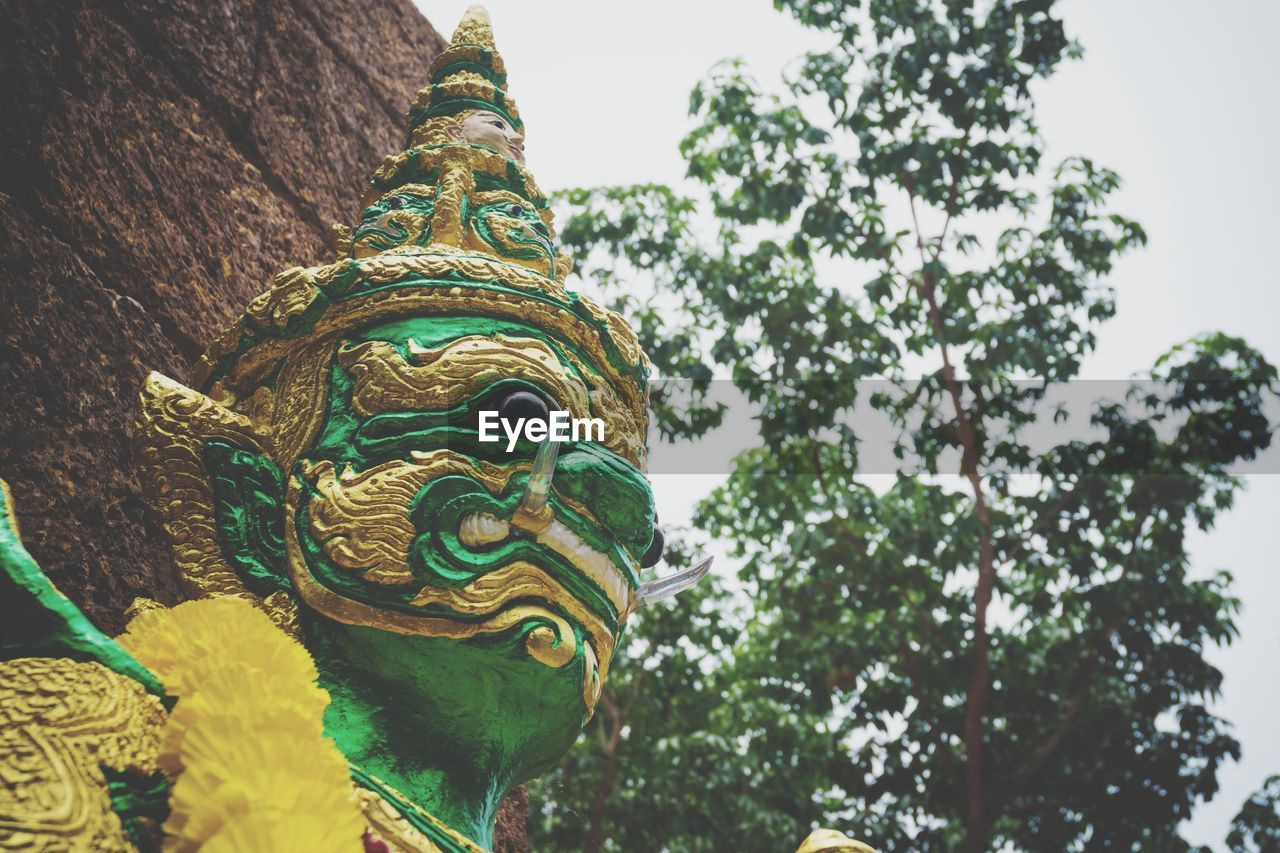 LOW ANGLE VIEW OF BUDDHA STATUE AGAINST TREES