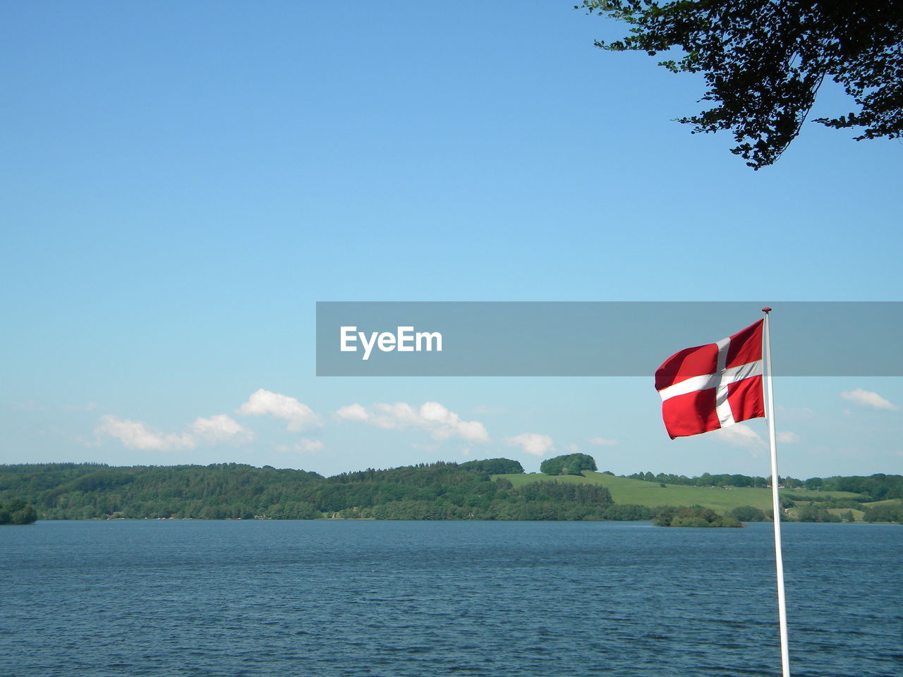 Danish flag by sea against blue sky