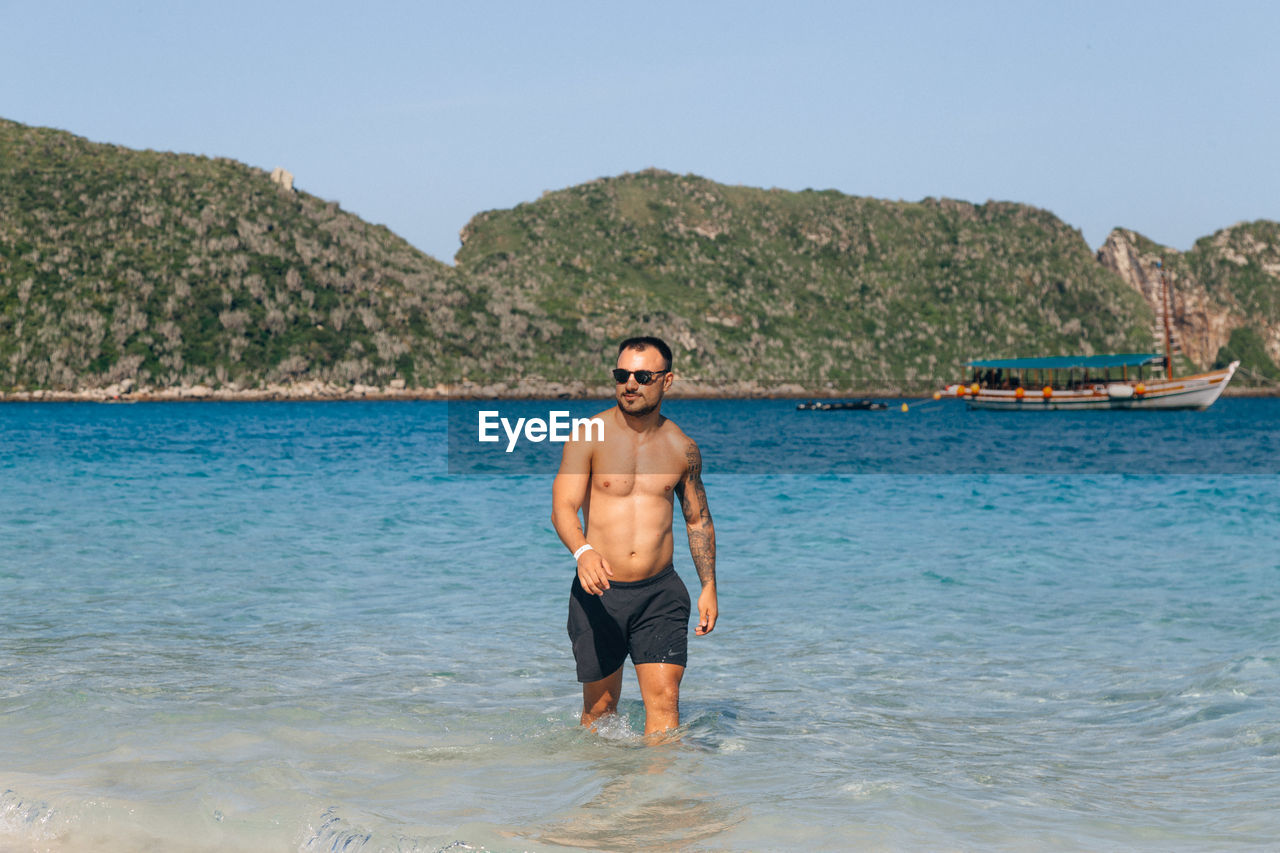 Shirtless young man walking on beach