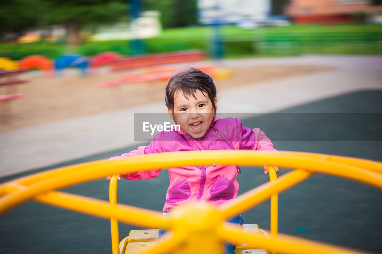 Portrait of happy girl sitting in outdoor play equipment