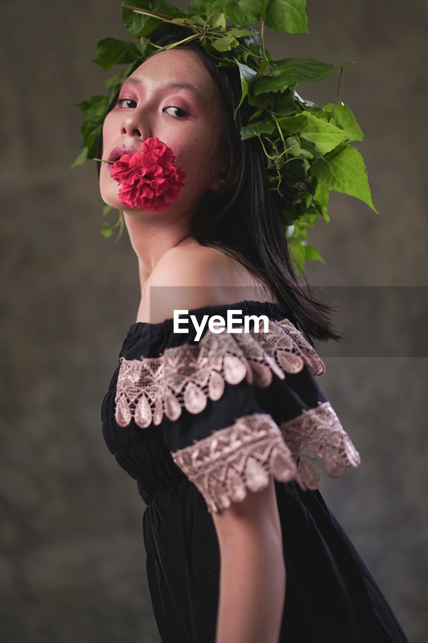 Portrait of young woman standing against red plant