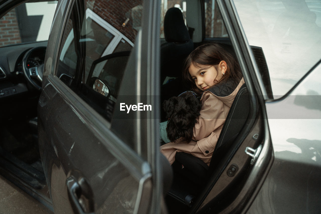 Portrait of young girl sitting  in car holding a dog