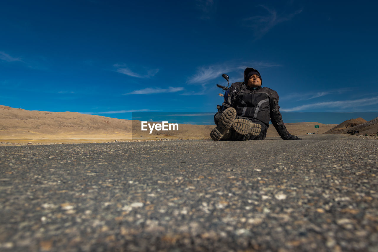 Man sitting on road at desert against sky