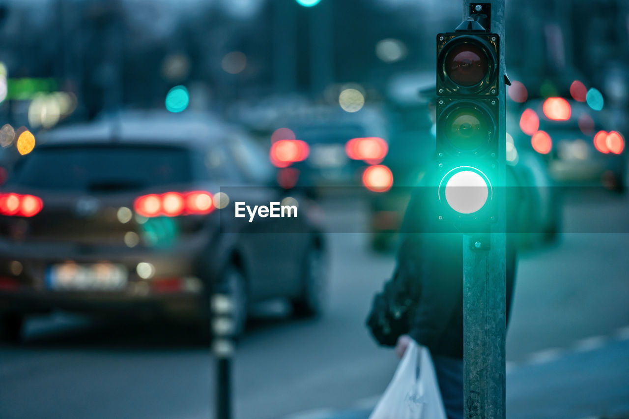 A city crossing with a semaphore on blurred background with cars in the evening streets, green light