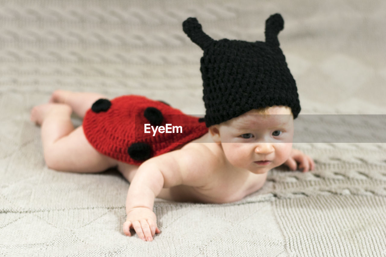 Full length of cute baby girl wearing knit hat while lying down on bed