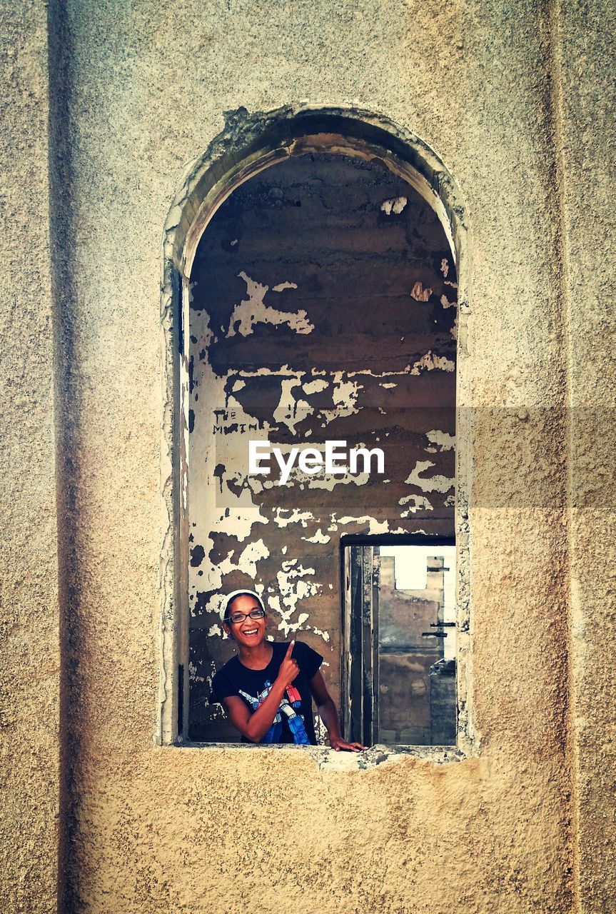 Portrait of smiling young woman at old building window