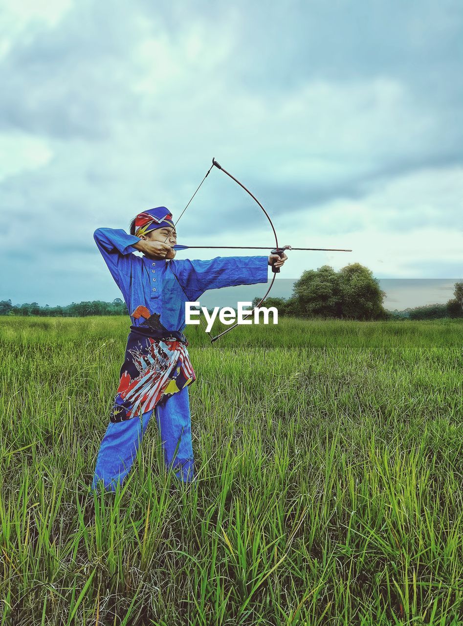 Side view of child standing on field with a bow and arrow like a malay worrior 