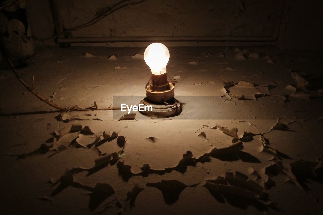 Low angle view of illuminated electric bulb on weathered wall