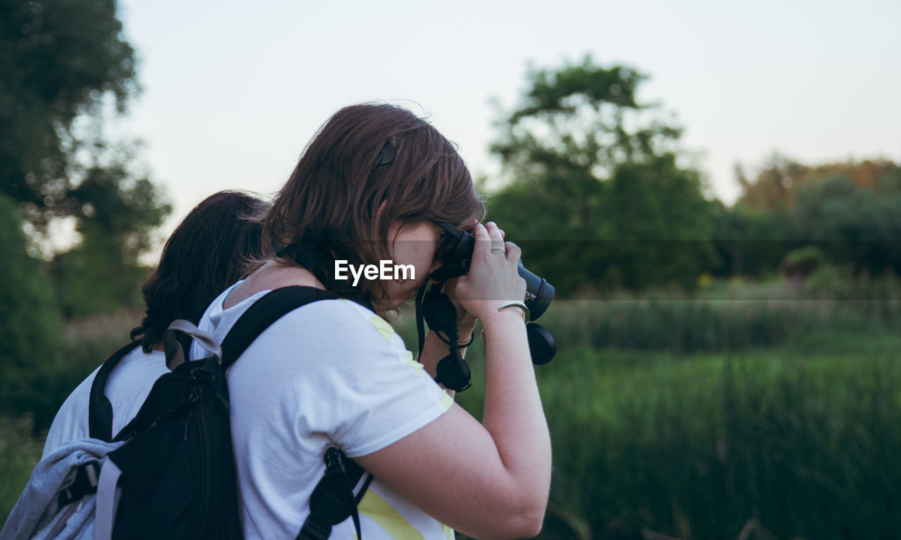 WOMAN PHOTOGRAPHING WHILE HOLDING CAMERA ON FIELD