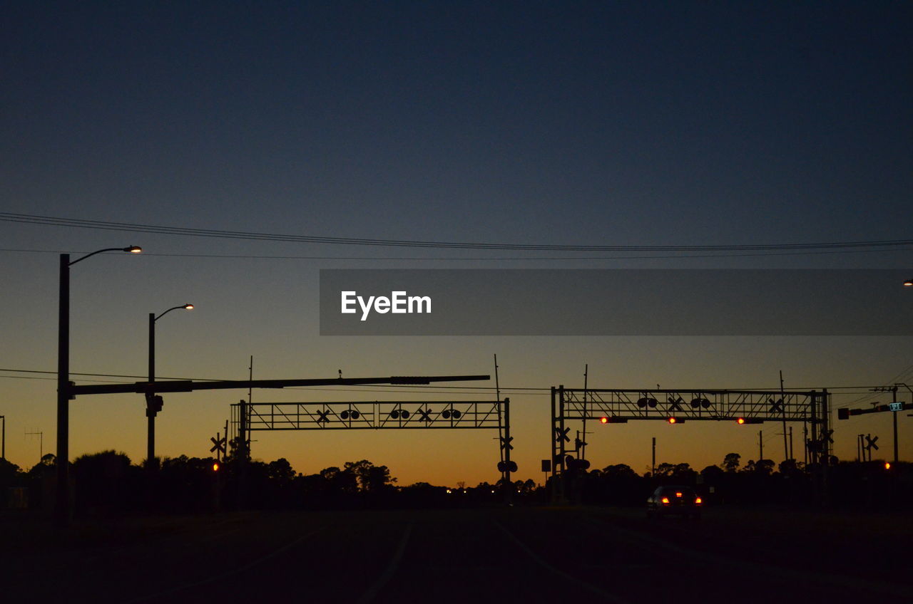 Silhouette of railroad crossing and road at sunset