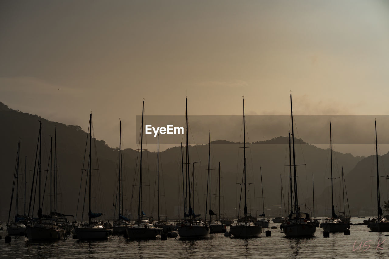 Sailboats moored at harbor against sky during sunset