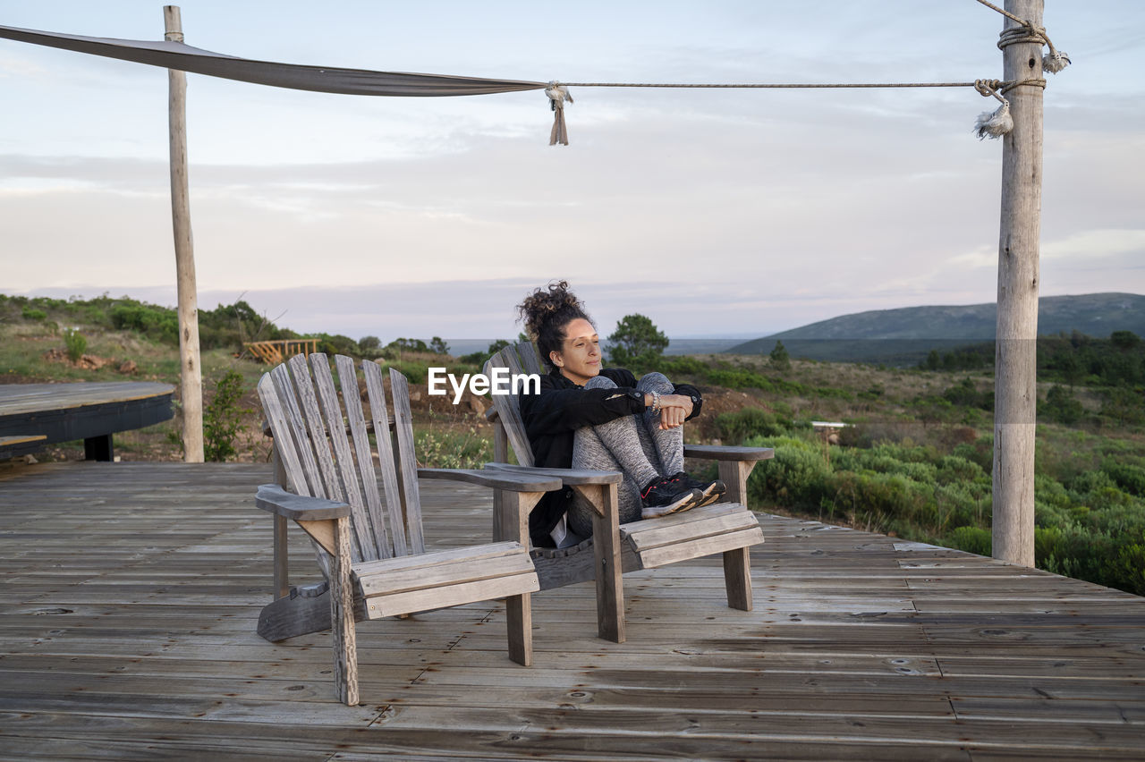 Relaxed woman sitting on a deck in the nature during sunset.