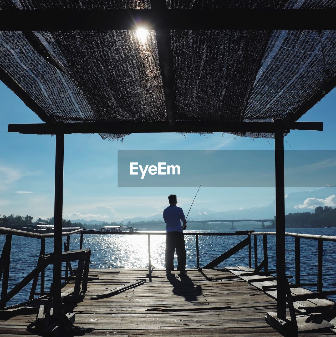 FULL LENGTH REAR VIEW OF MAN STANDING ON RAILING AGAINST SEA