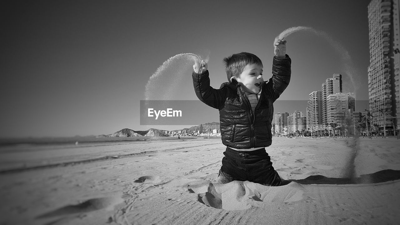 Boy playing with sand on beach against clear sky