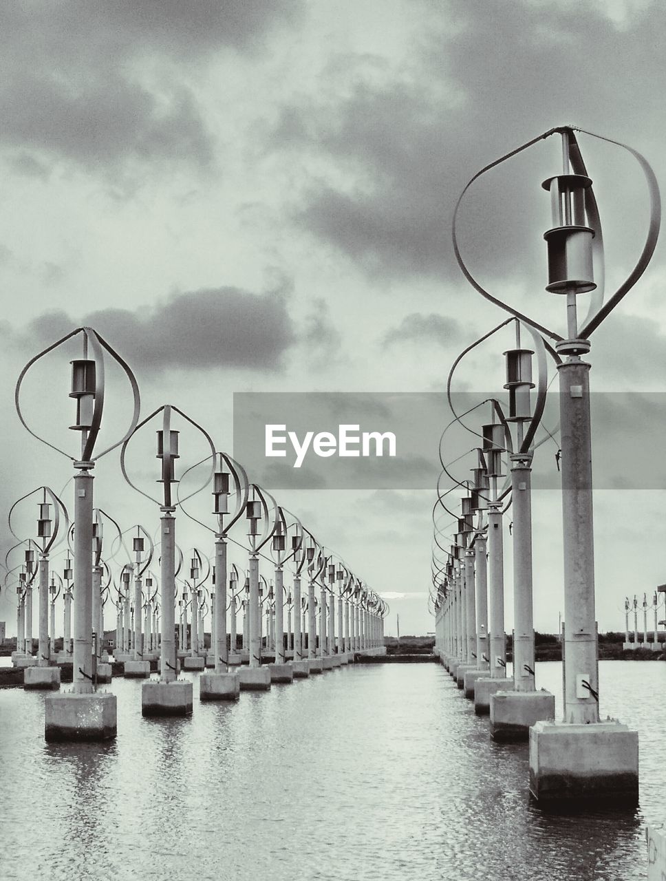 Street lights on pier by river against sky