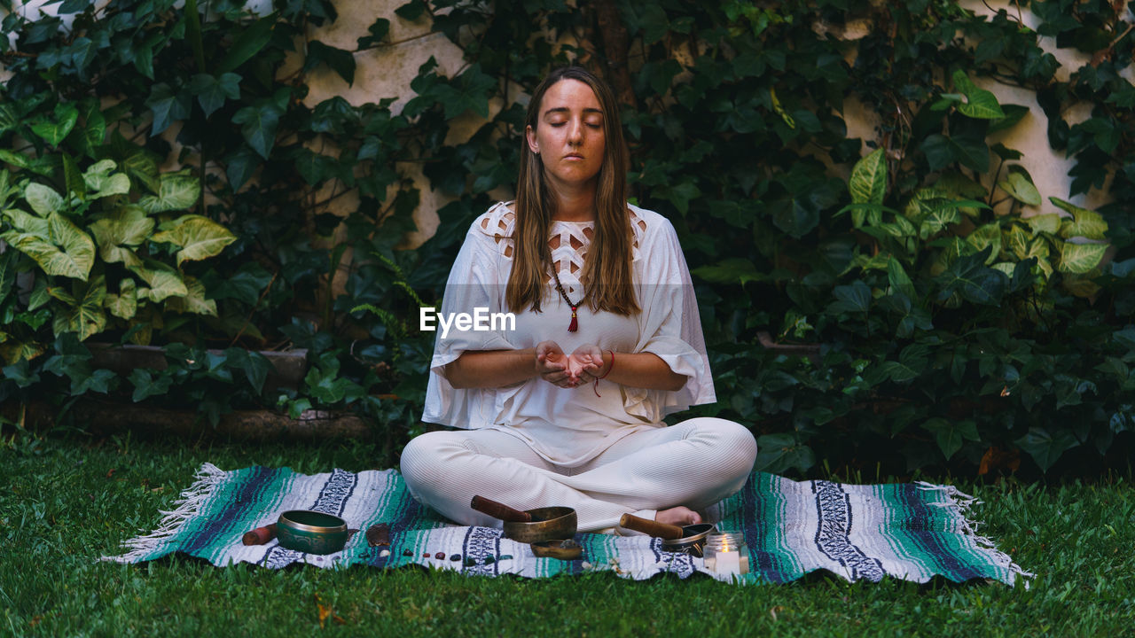 Full length of young woman meditating while sitting outdoors