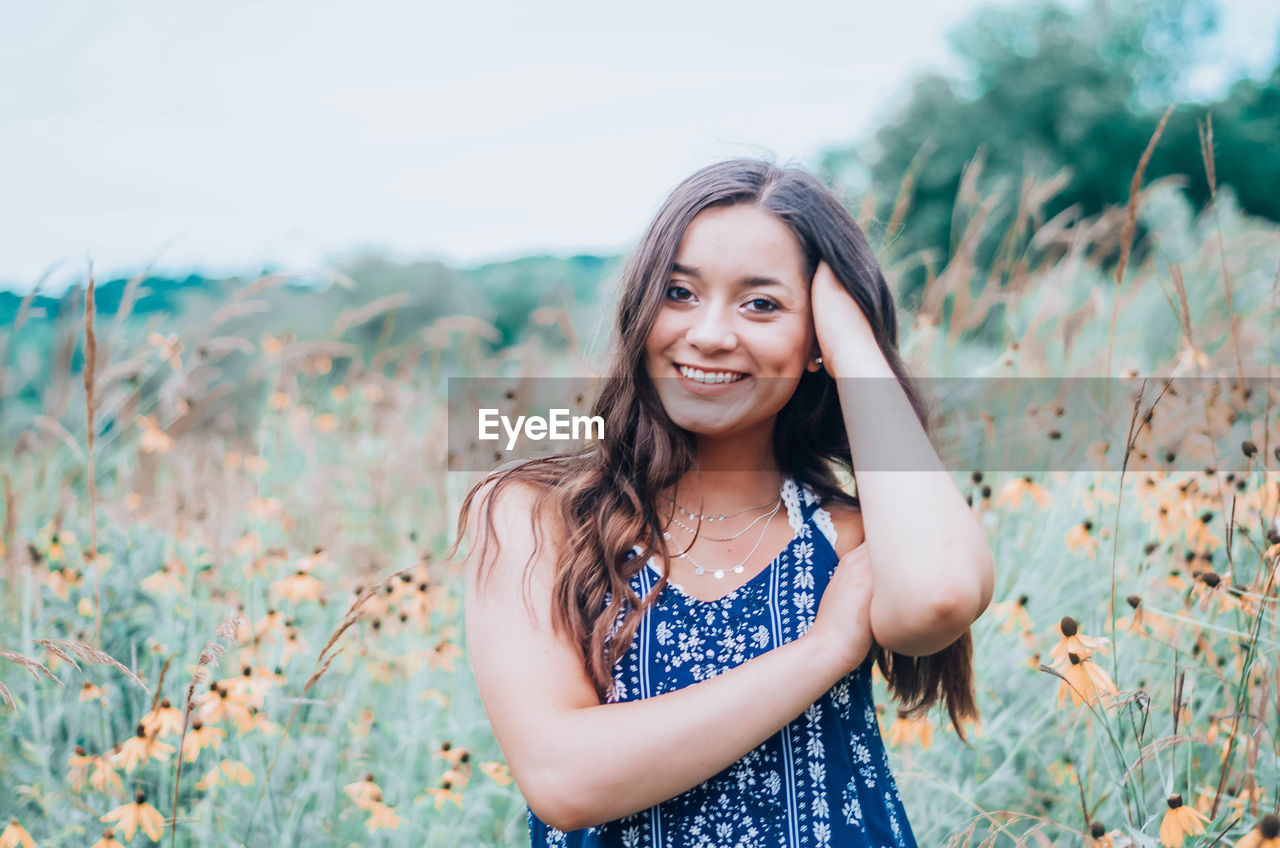 Portrait of smiling young woman standing on field against sky