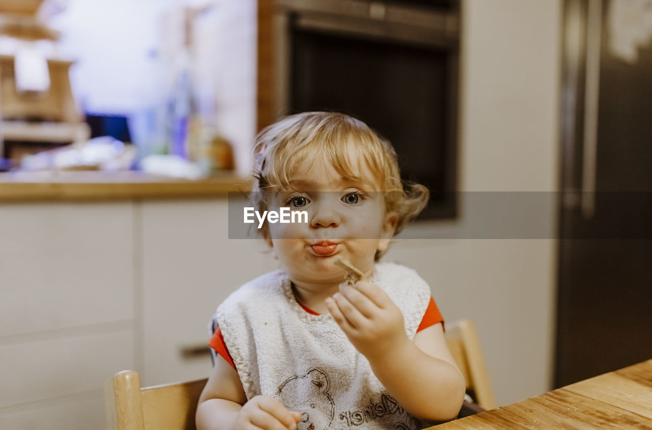 Close-up portrait of cute baby girl eating cookie at home