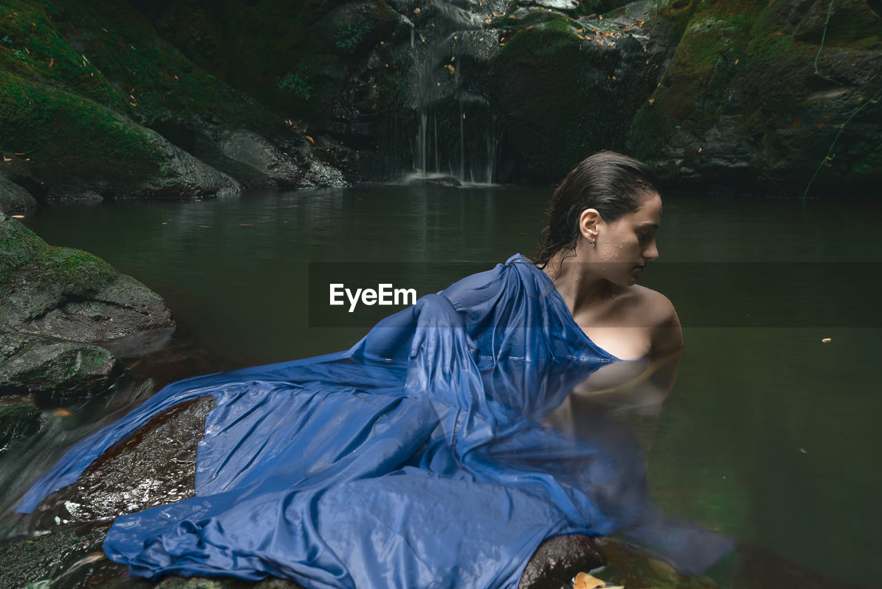 Young woman standing in lake against waterfall