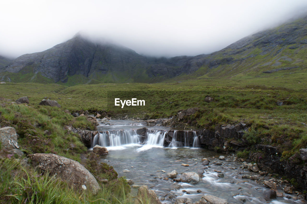 SCENIC VIEW OF WATERFALL AGAINST MOUNTAIN