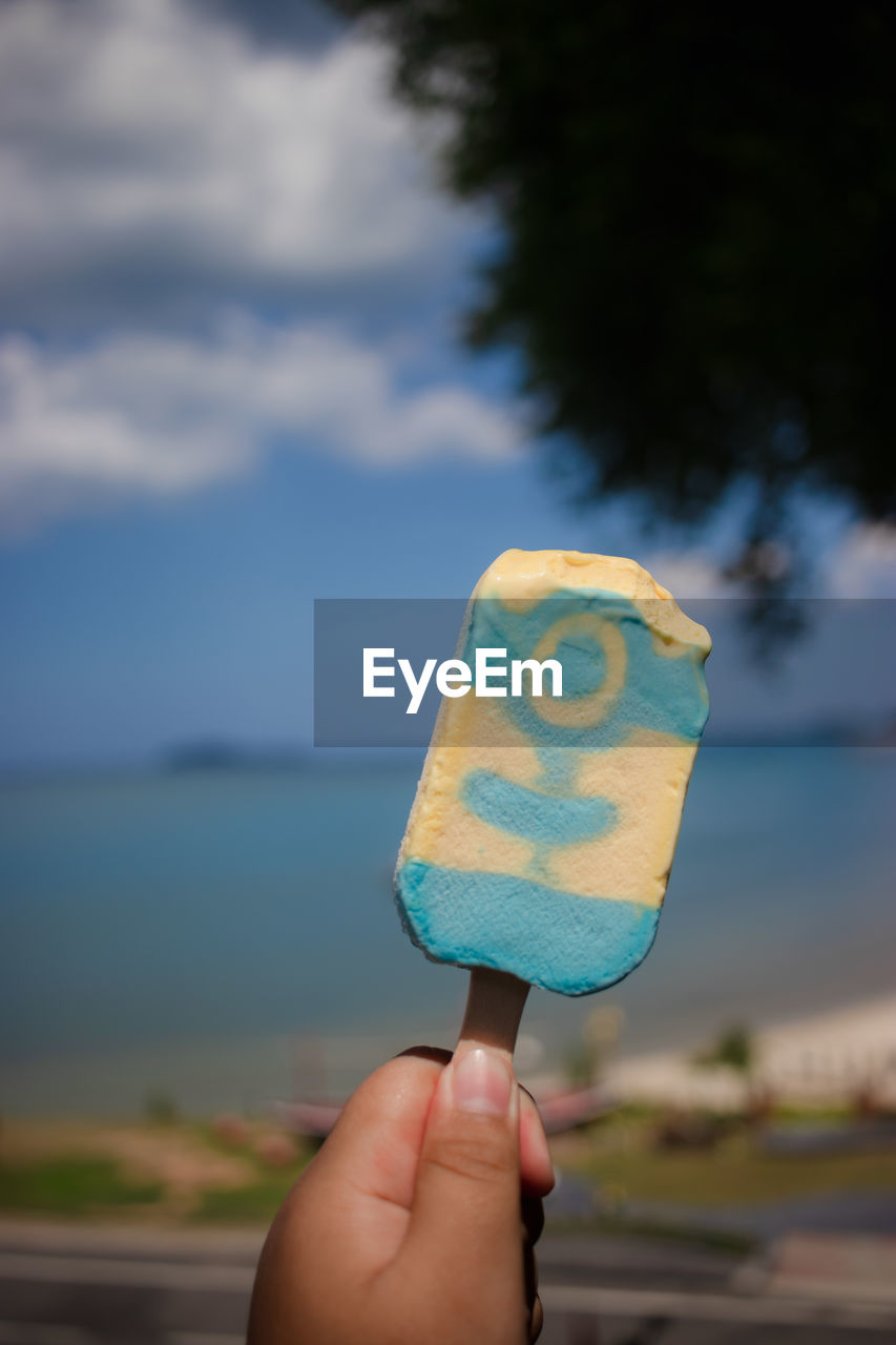 Close-up of hand holding ice cream cone against sky