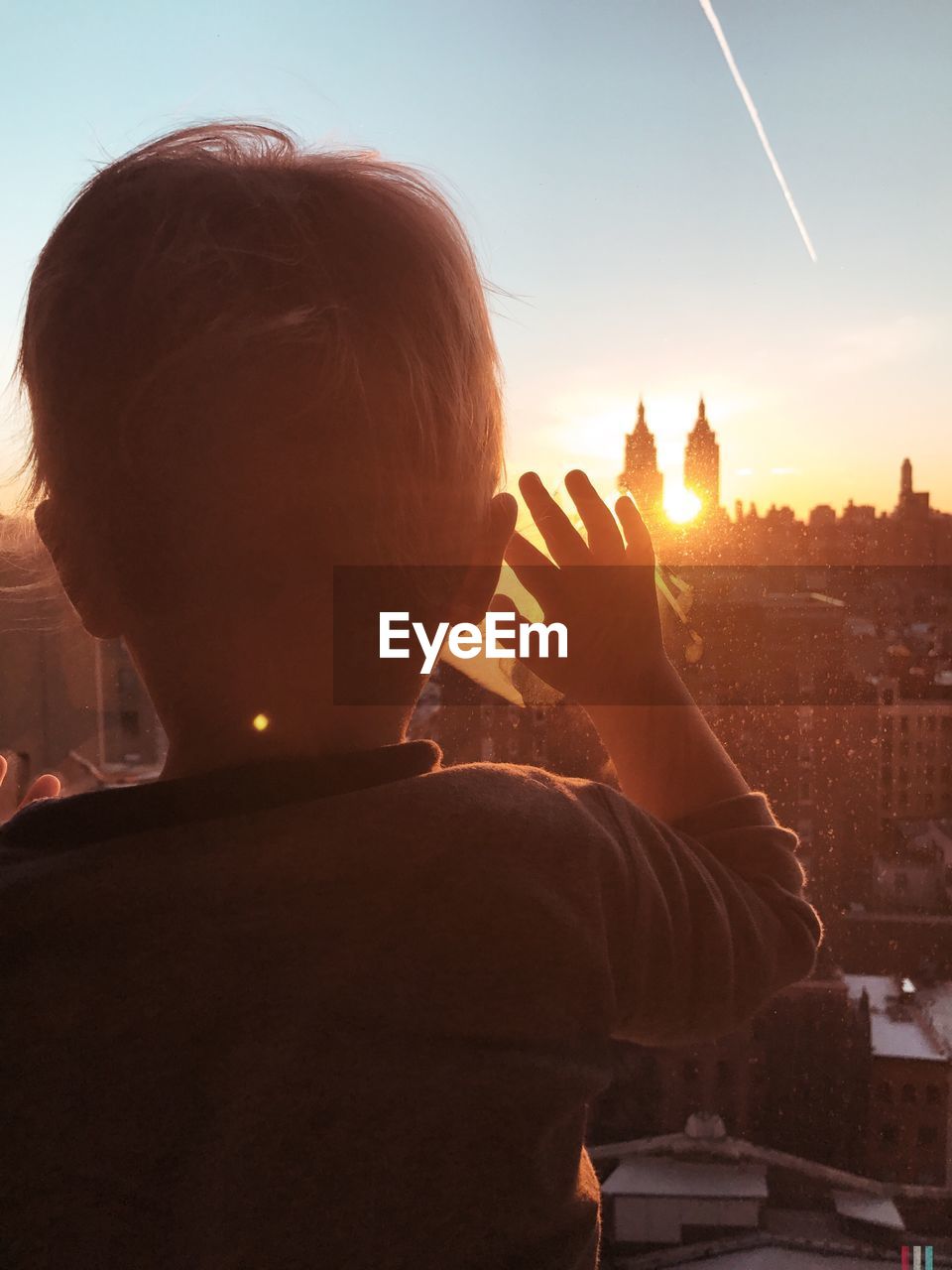 Rear view of boy standing by window against the san remo during sunset