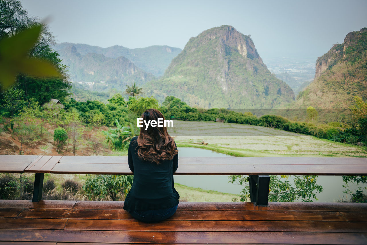 Rear view of woman sitting on mountain against sky