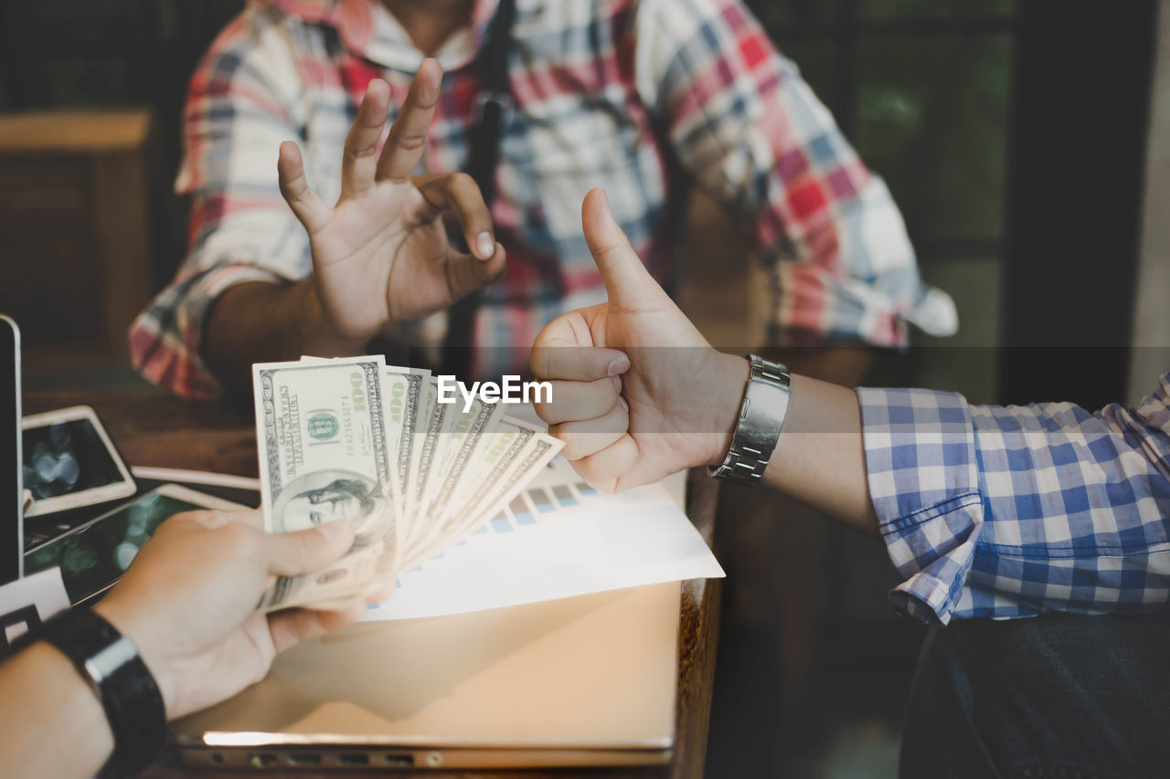 Cropped hand holding paper currency by colleagues gesturing on office desk