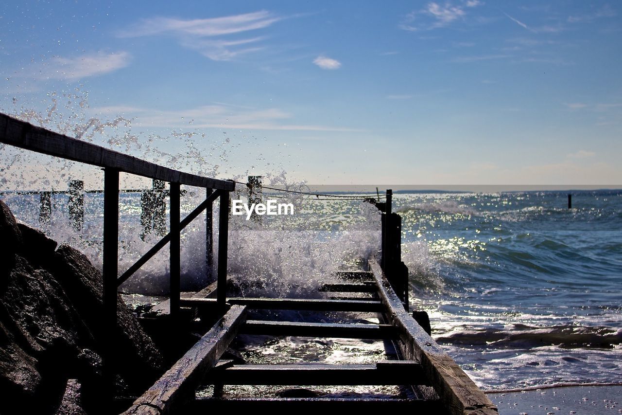 Waves splashing on old damaged pier on sea against sky