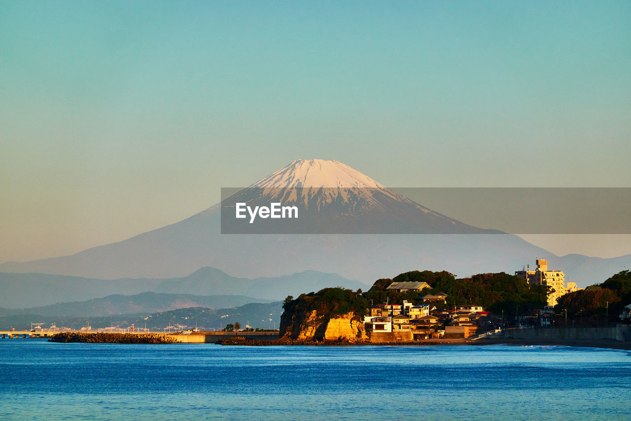 Scenic view of sea and snowcapped mountains against clear blue sky