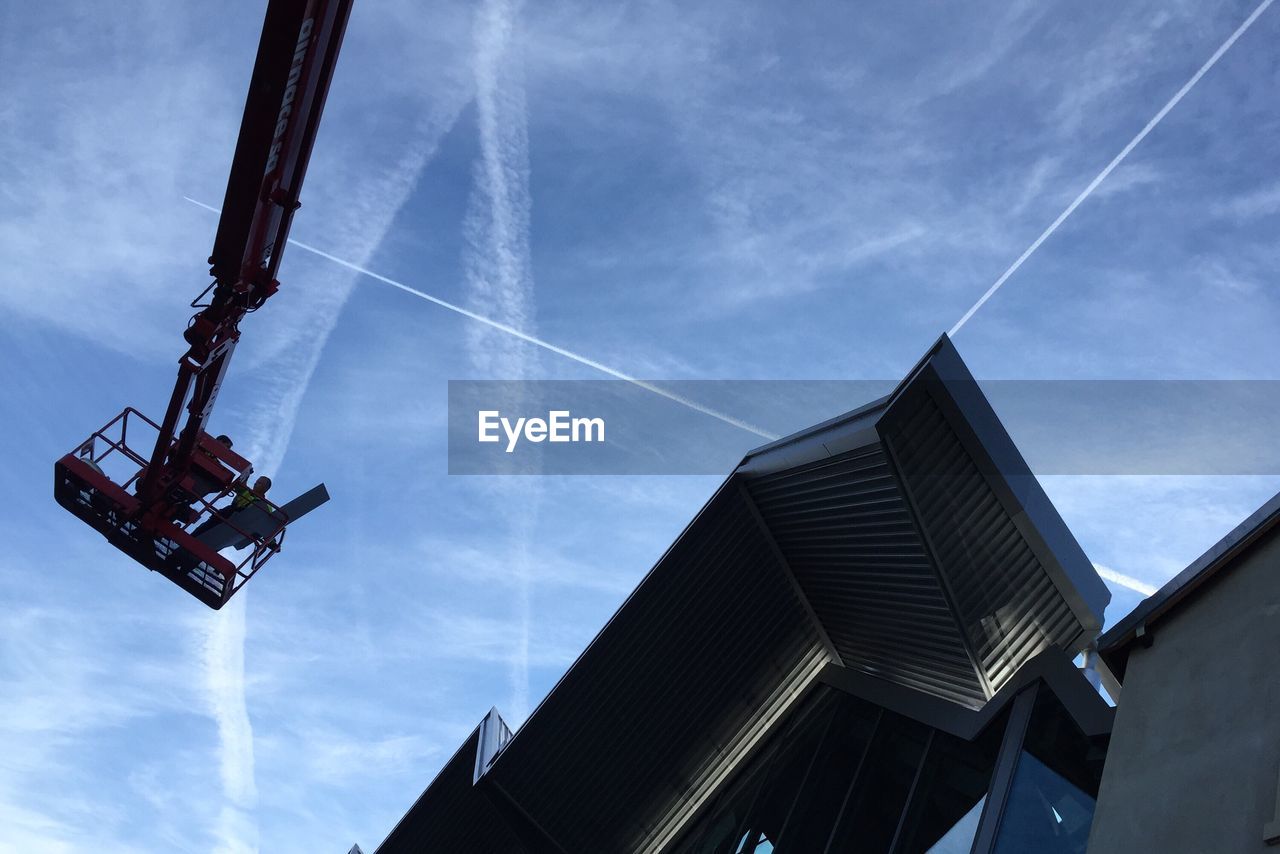 Low angle view of cherry picker and building against sky