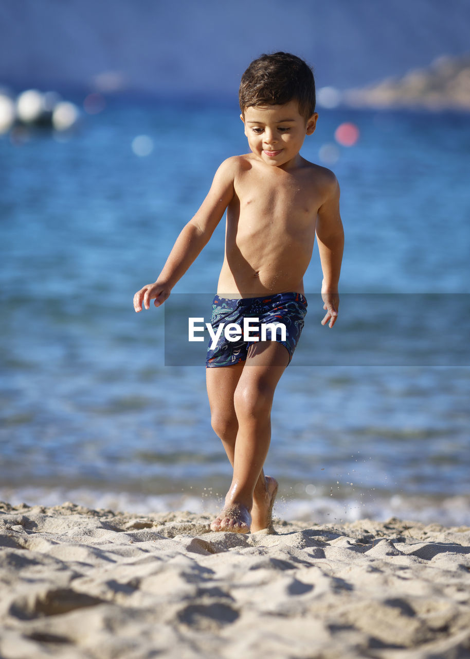 full length of shirtless boy playing in sea