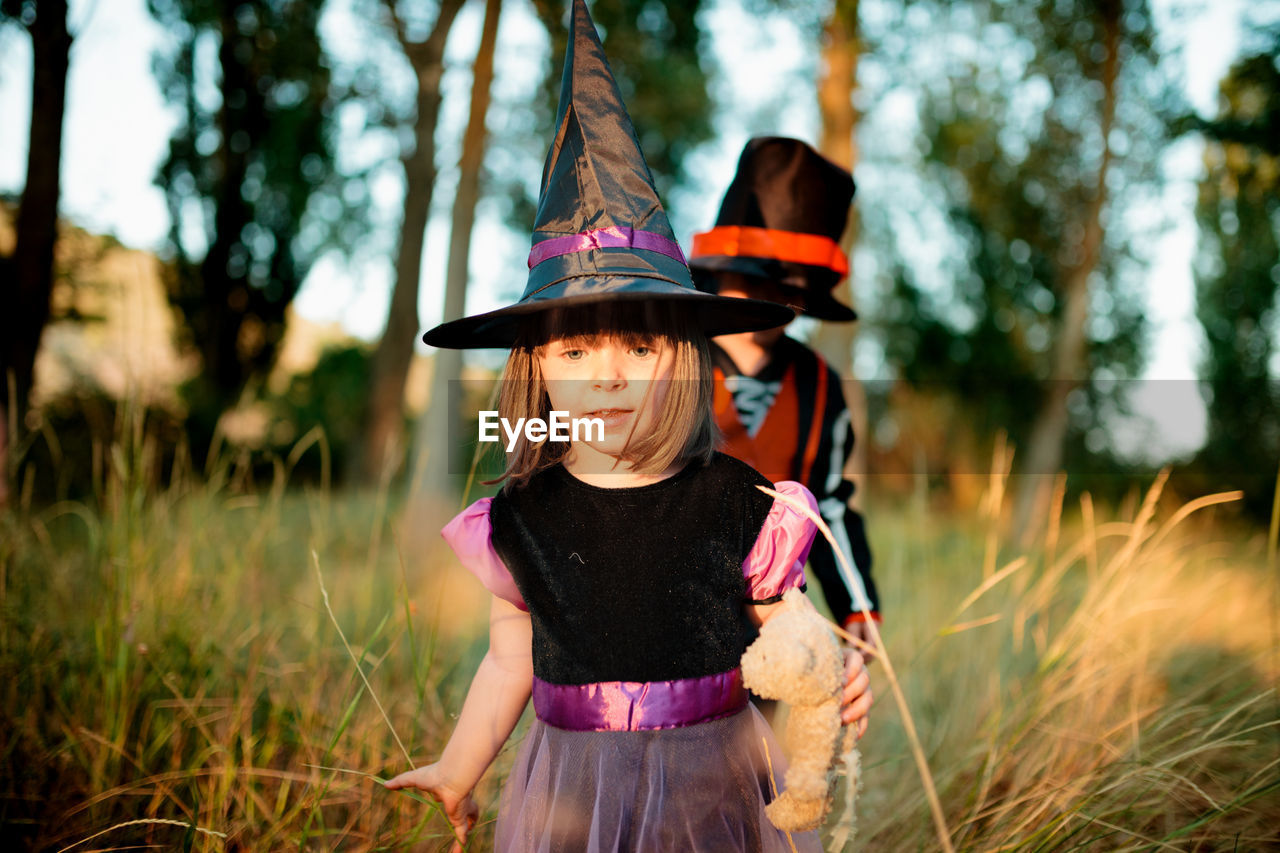 Cute siblings in costume against trees during halloween