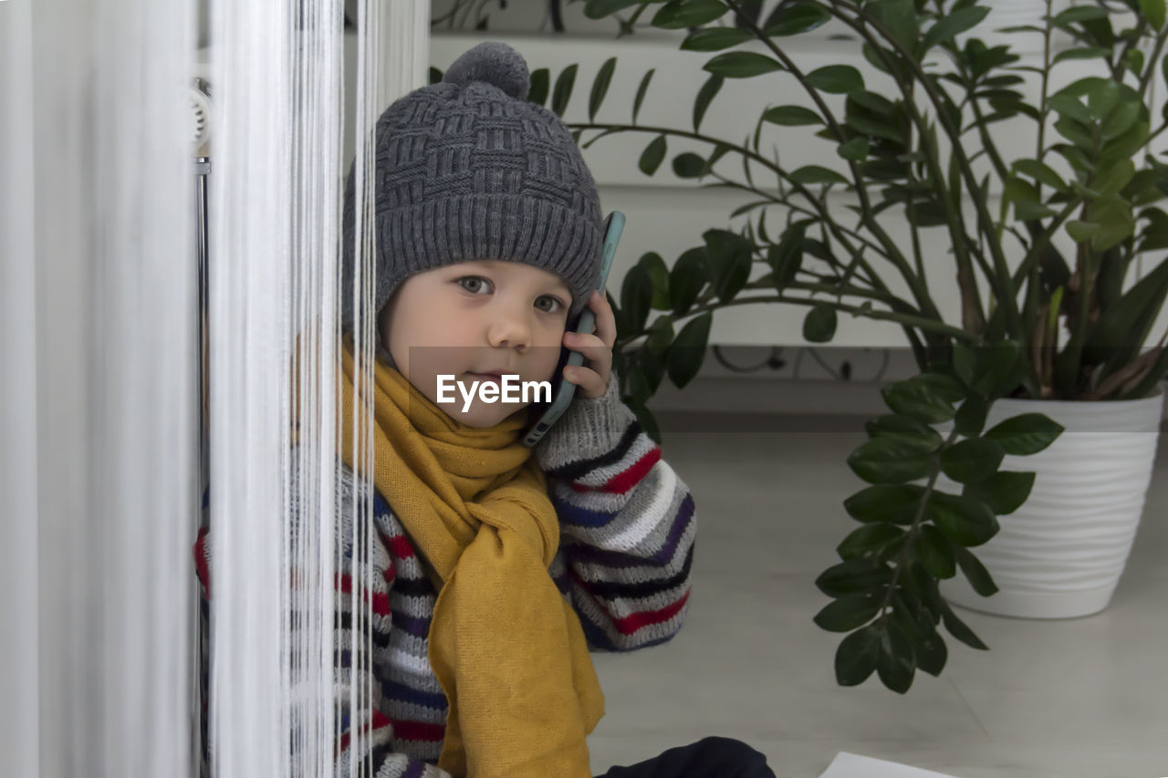 A small child with a yellow scarf near the radiator speaks on the phone.  energy crisis concept