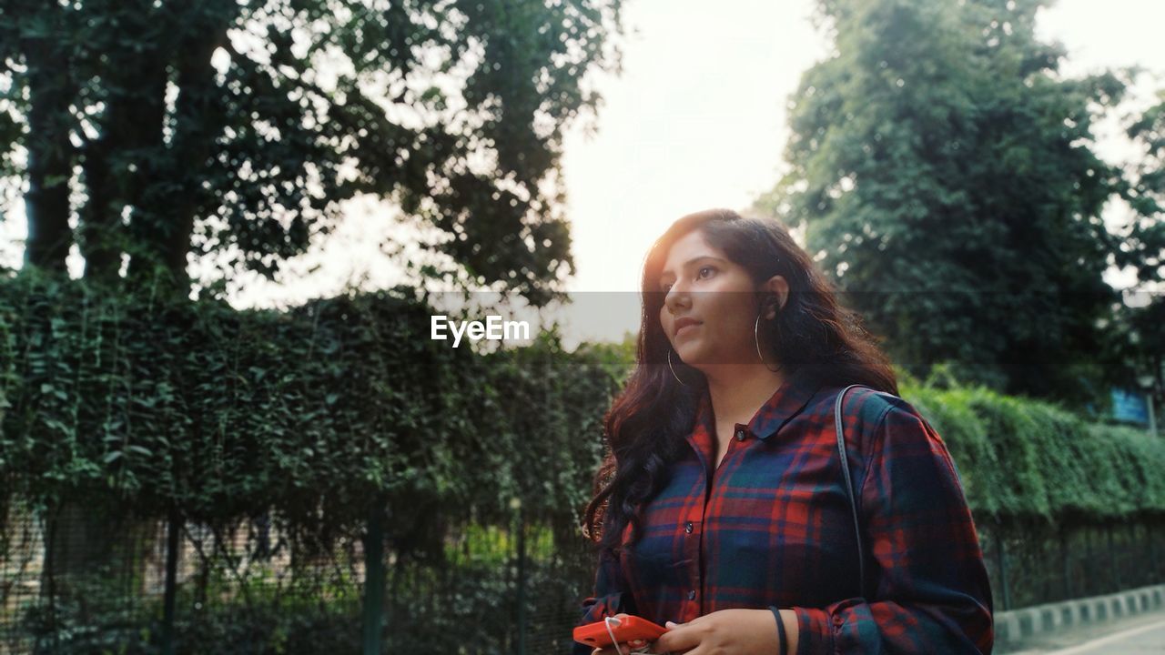 Young woman looking away against trees