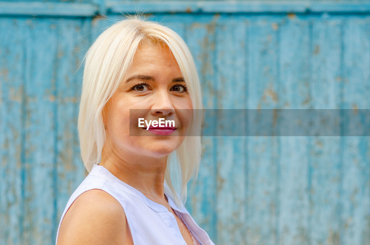 Portrait of smiling well-groomed middle-aged woman. blonde. bright makeup. blurred blue background