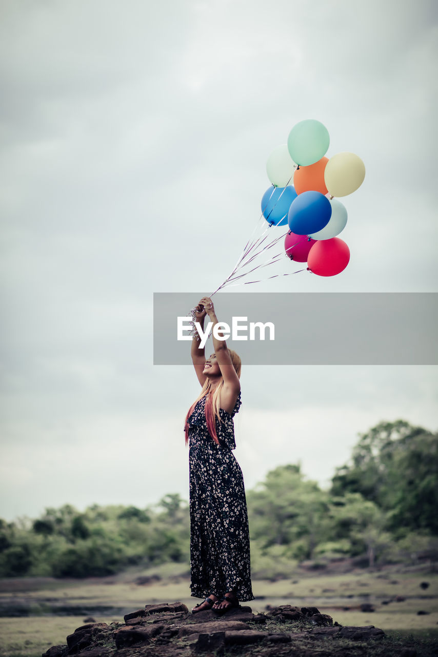 Full length of woman holding balloons while standing against sky