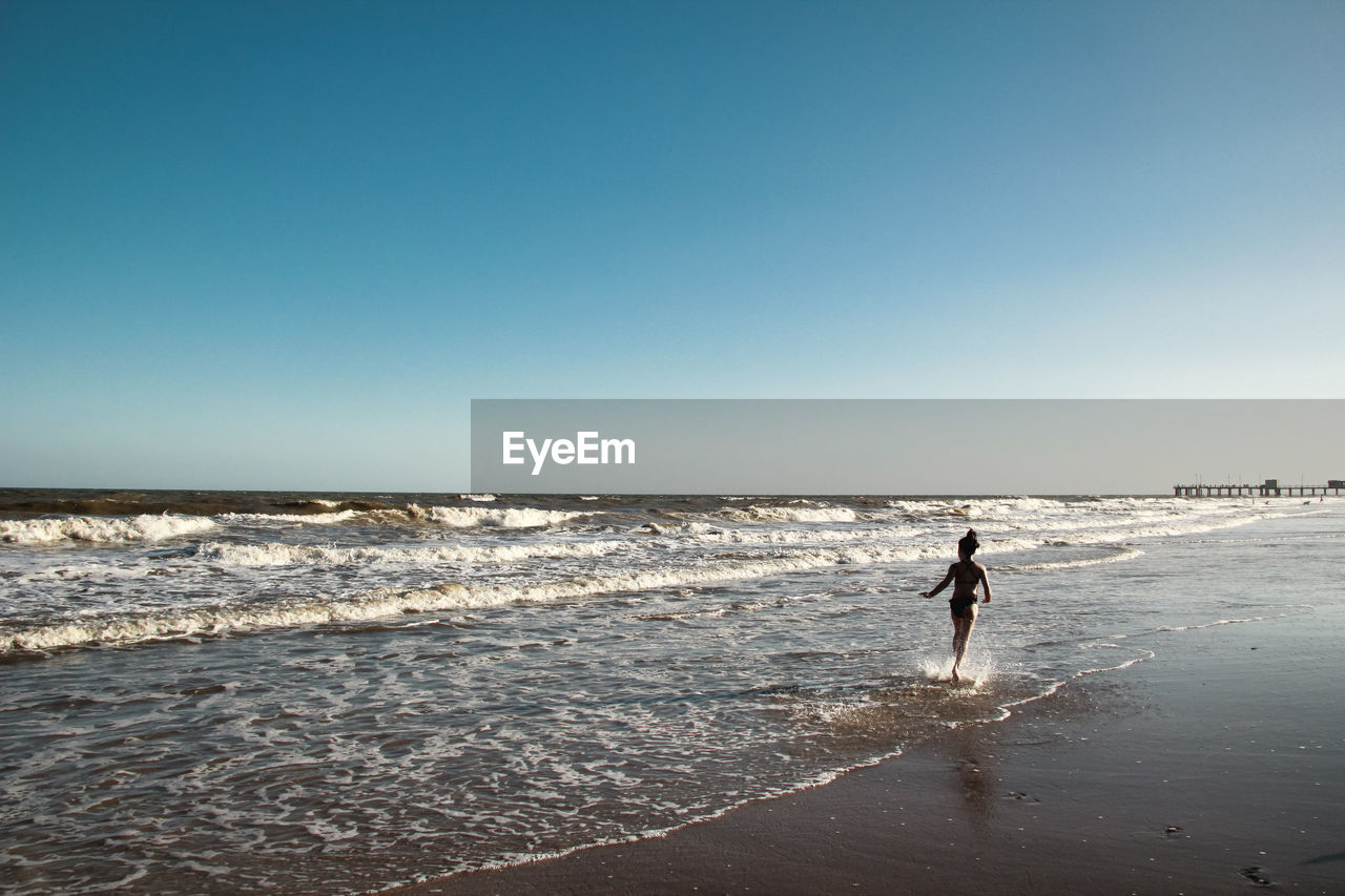 Rear view of girl running at shore against clear sky