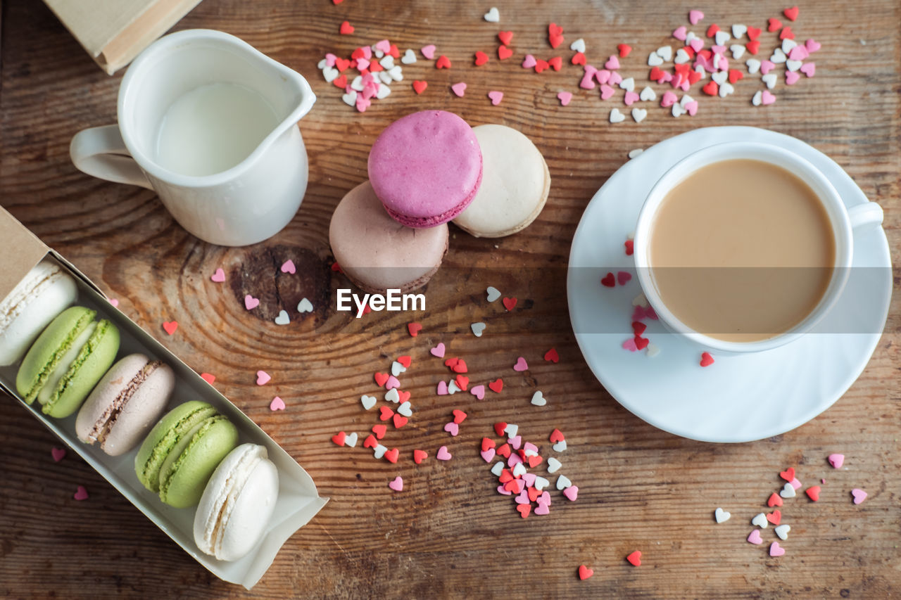 Macaroons in a box, a cup of coffee, a milk jug against the background of small hearts 