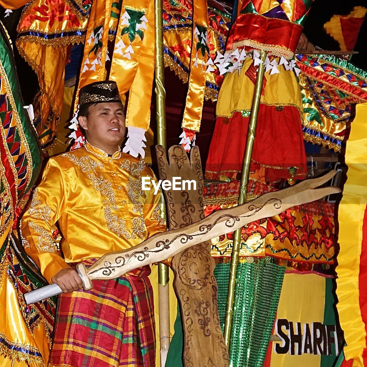 FULL LENGTH OF SENIOR MAN IN TRADITIONAL CLOTHING HOLDING CAMERA