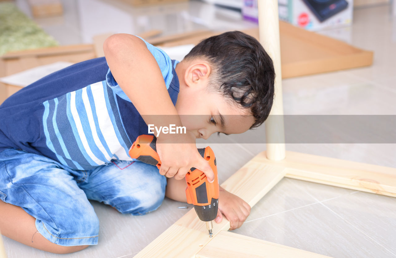 Boy drilling wood at home