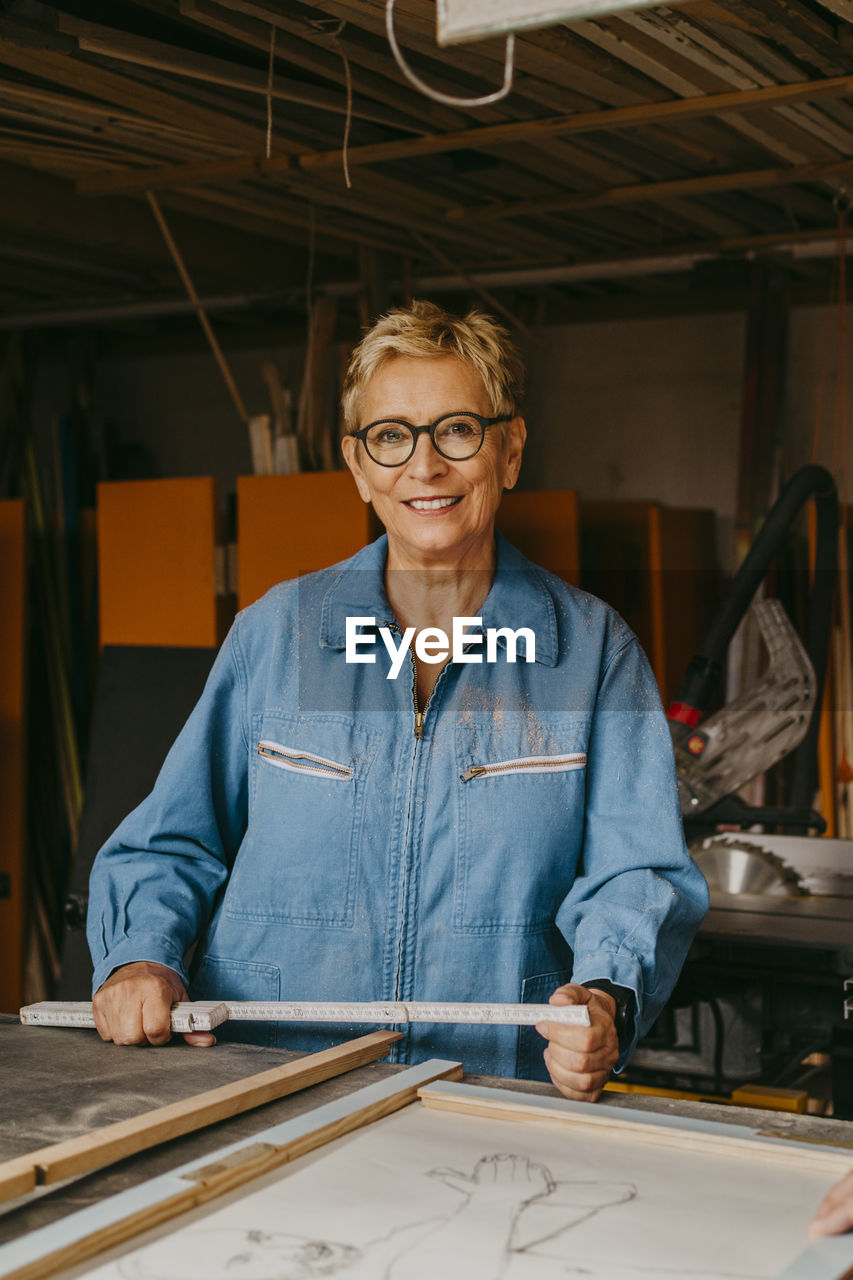 Portrait of smiling senior craftswoman with measuring tape at workshop